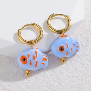 Dettaglio di orecchini a forma di pesce in ceramica blu con motivi dipinti in arancione