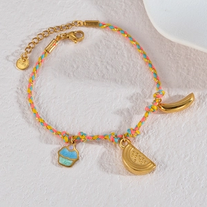 Close-up of woven rope bracelet with gold cupcake and fruit charms on white background