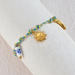 Detail of woven rope bracelet featuring golden sun, moon charms and ceramic bead
