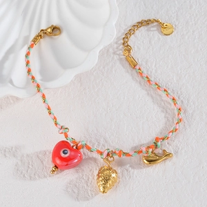 Detail of woven bracelet with gold strawberry, heart, and whale charms on white background