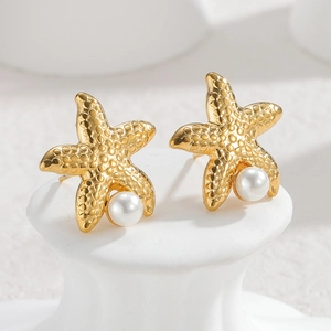 Golden starfish stud earrings with white pearl detail on minimalist white stand