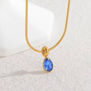 Macro shot of gold snake chain with water-drop blue zircon pendant on stone surface