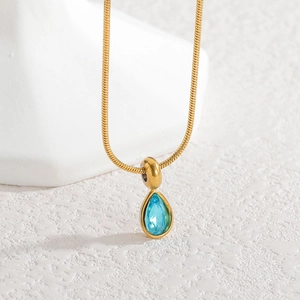 Macro shot of gold teardrop pendant with blue zircon stone on minimalist snake chain