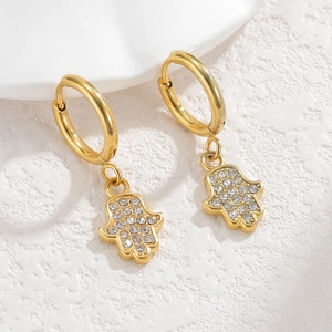 Detailed view of gold Hamsa hand earrings with clear zircon stones on a white stone base