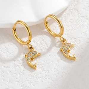 Close-up of gold dolphin earrings with micro-set rhinestones on textured surface