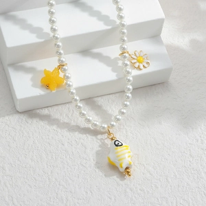 Détail collier en perles avec pendentifs marguerite, étoile de mer et poisson sur décor blanc