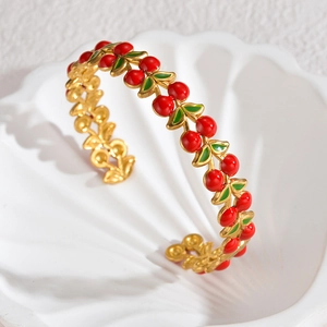 Gros plan d'un bracelet ouvert cerise avec perles rouges et feuilles en émail vert