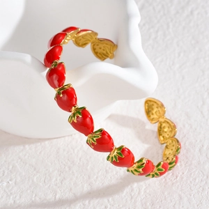 Détails des motifs fraises en émail sur un bracelet jonc doré poli élégant