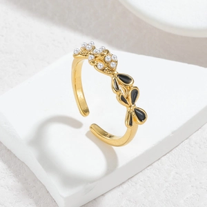 Macro view of gold ring featuring black enamel bow and small white pearl inlay