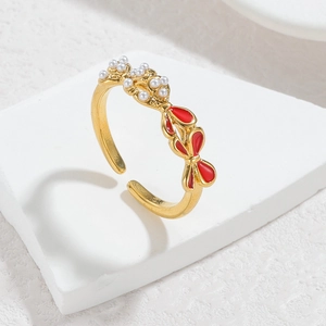 Close-up of golden bow ring with red oil drip detail and white inlaid pearls on a white base
