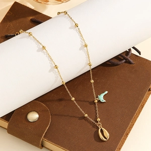 Detail view of golden bead chain necklace featuring a blue dolphin and a conch shell pendant