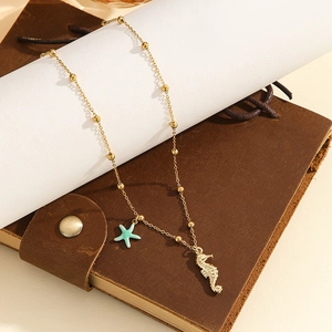 Golden bead necklace with ocean starfish and seahorse charms on a leather notebook
