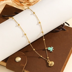 Detail of gold beaded chain with mint green fish and ribbed seashell charms