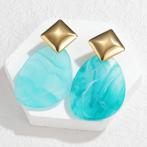 Close-up of geometric acrylic drop earrings with marble texture on white podium