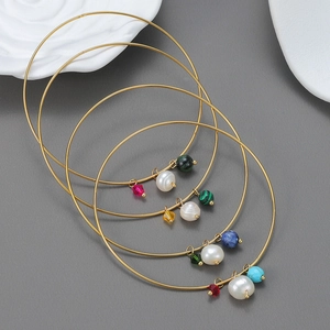 Gold-plated bangles set with colorful gemstones, pearls and pendants on grey surface