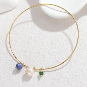 Detail of gold titanium bangle with blue stone, white pearl, and green crystal charms
