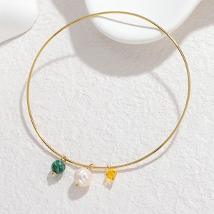 Detail of minimalist gold titanium bangle featuring malachite, pearl, and crystal charms
