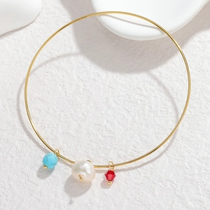 Detail of a thin gold bangle with turquoise bead, white pearl, and red faceted pendant