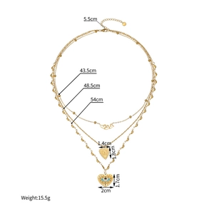 Collier multicouche doré avec pendentifs en forme de cœur et œil grec sur fond blanc