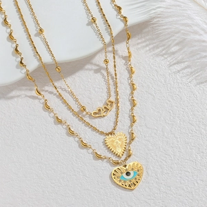 Collier doré à trois couches avec cœur, médaille et pendentif œil bleu sur fond blanc