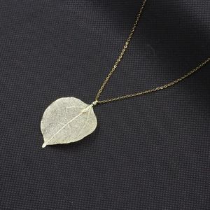 Pendentif feuille dorée élégant avec nervures délicates sur fond noir texturé de qualité