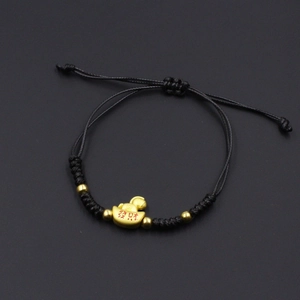 Macro detail of hand-woven black cord bracelet with gold charm and lucky red lettering