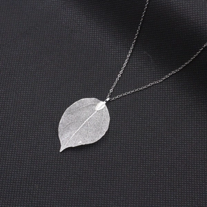Sautoir argenté avec pendentif feuille naturelle ajourée sur fond à carreaux noirs