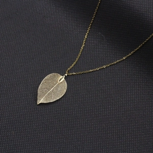 Détail macro du pendentif feuille dorée montrant les textures des nervures naturelles