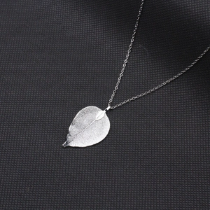 Vue détaillée du pendentif feuille argentée avec nervures naturelles et fine chaîne croisée