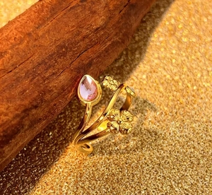 Detail of gold floral ring with pink pear-cut gemstone on rustic wood texture