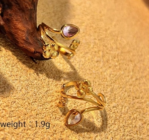 Detail of gold bypass rings featuring purple and clear teardrop gemstones and floral reliefs