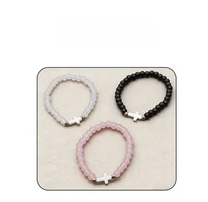 Close-up of glass bead bracelets featuring cross charms in white, black, and pink colors