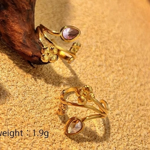 Golden open ring featuring 3D flowers and light purple gemstone on a textured background