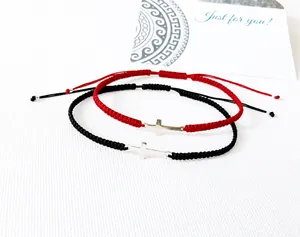 Detail of handmade woven couple bracelets with silver cross charm in red and black