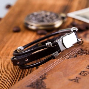 Macro shot of dark brown multi-layer leather bracelet with silver metal clasp on wood