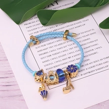 Close-up of light blue braided bracelet with gold crown, umbrella, and high heel charms