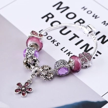 Close-up of silver snake chain bracelet featuring pink beads and purple flower pendant