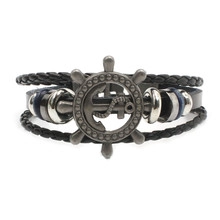 Detailed macro view of black multi-layer leather bracelet with silver anchor and helm charm