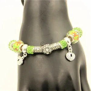 Détail d'un bracelet de perles avec perles pavées vertes et pendentifs cœur sur main noire