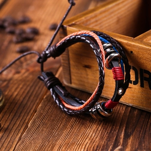 Retro handmade braided cowhide leather bracelet with metallic rings on a rustic wooden box