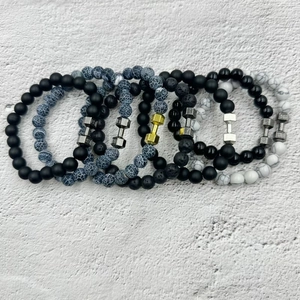 Detail of beaded fitness bracelets with metal dumbbell charm on textured background