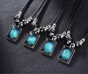 Détail de quatre colliers pendentifs zodiaque avec cordons en cuir sur fond noir mat