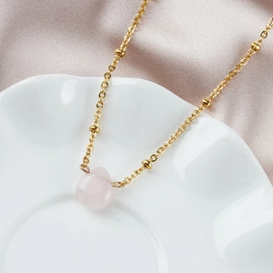 Detail of a thin gold necklace with a pink waterdrop gemstone on a white silk background