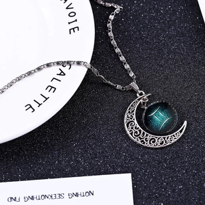 Silver Gemini moon necklace with blue starry glass gem on black glitter background