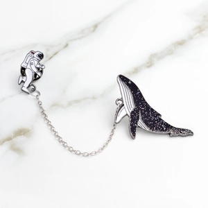 Detail of creative astronaut and whale enamel pin set with a connecting silver chain