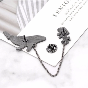 Minimalist whale and diver enamel pin set with link chain on a marble surface