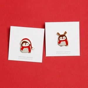 Detailed macro of Christmas penguin and reindeer enamel pins on white cardboards
