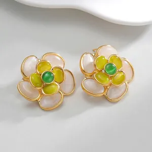 Macro shot of gold-plated flower earrings with white petals and green crystal centers