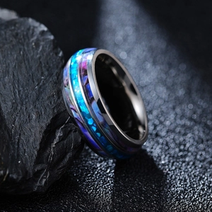 Makroaufnahme eines breiten Titanrings mit bunter Abalone-Einlage auf grauem Stein