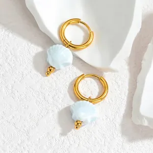 Detail of gold seashell earrings with light blue pendants on a textured stone surface